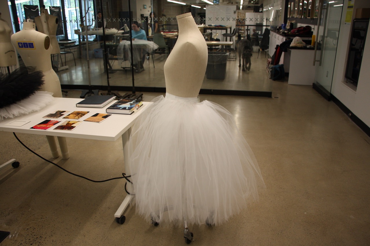 photo of exhibition studio, close up of a tutu in progress, blurred students working in background